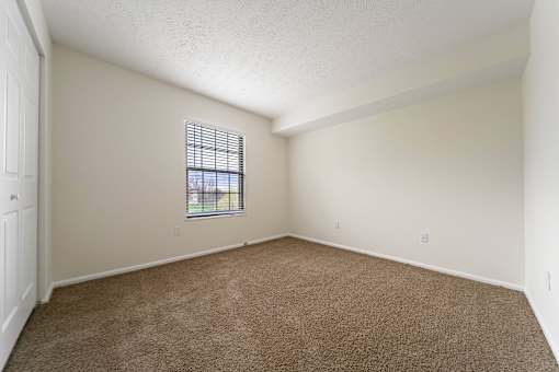 A room with a carpeted floor and a window with blinds at Hunt Club Apartments, Copley, Ohio