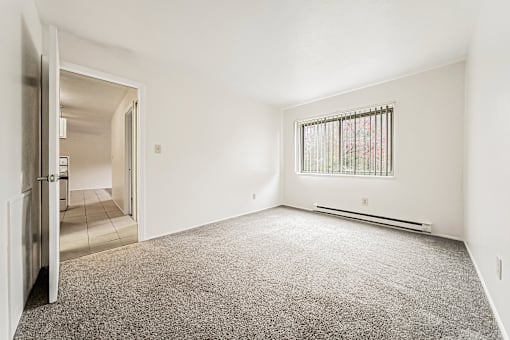 A room with a carpeted floor and a window with bars.