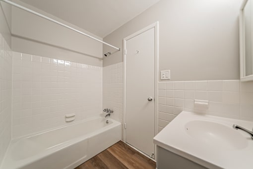 A white bathroom with a tub, sink and mirror.