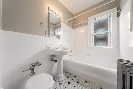 A white sink and toilet in a bathroom with a window at Heights Collection Apartments, Cleveland Heights 44106