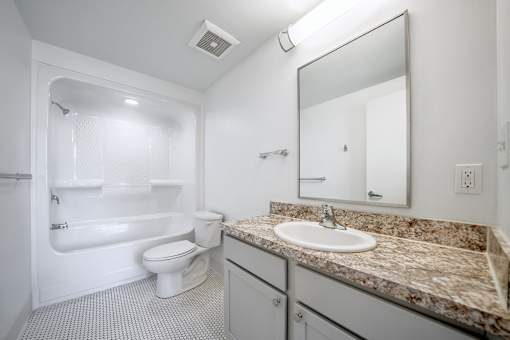 A white bathroom with a granite counter top and a white toilet.
