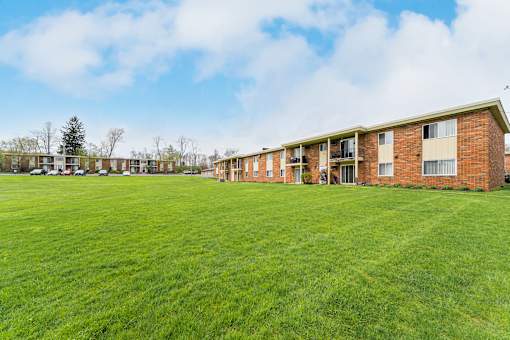 A grassy field in front of a brick building with cars parked in the background at Integrity Chardon Apartments,Ohio, 44024