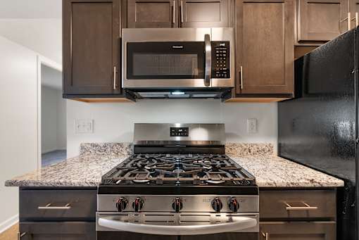 A black stove top oven with four burners and a stainless steel microwave above it at Integrity Medina Apartments, OH, 44256
