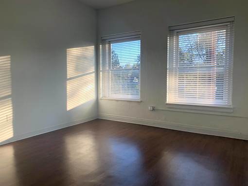 A room with wooden floors and two windows with blinds.