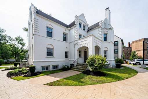 A white two-story house with a black roof and a brick walkway in front.