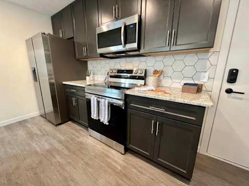 A kitchen with black cabinets and a stainless steel refrigerator.