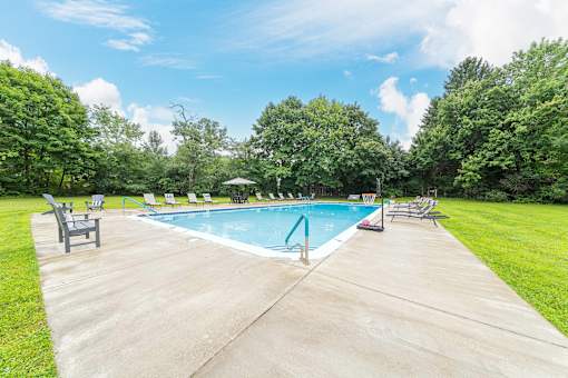 A swimming pool surrounded by trees and lawn chairs.