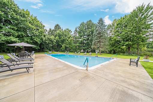 A large outdoor swimming pool surrounded by trees and lounge chairs.