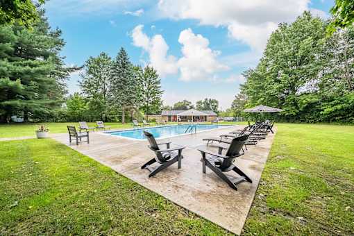 A pool surrounded by lawn chairs and trees.