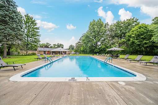 A large outdoor swimming pool surrounded by trees and lounge chairs.