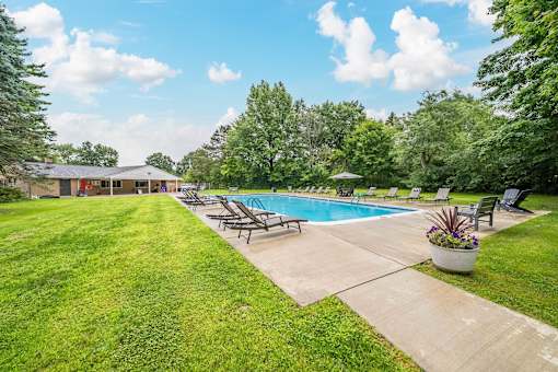 A pool surrounded by lawn chairs and trees.