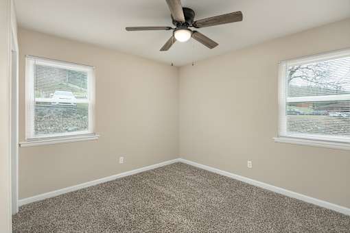 A room with a ceiling fan and two windows.