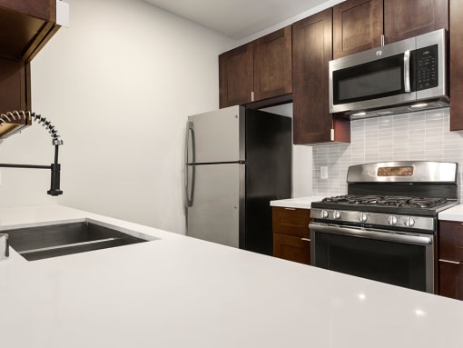 White tiled kitchen with modern faucet, stainless steel appliances, and refrigerator.
