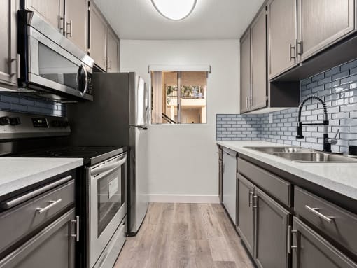 White tiled kitchen with stainless steel oven, microwave, and fridge..