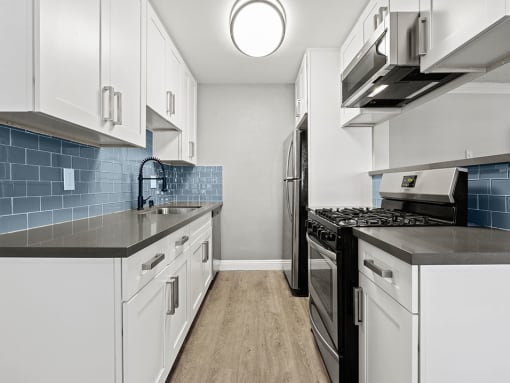 Blue tiled kitchen with stainless steel fridge, oven, and microwave.