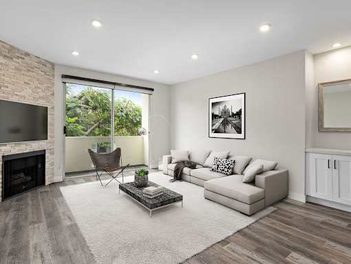 Hardwood floored living room with view of stone accent wall, fireplace, and private balcony.