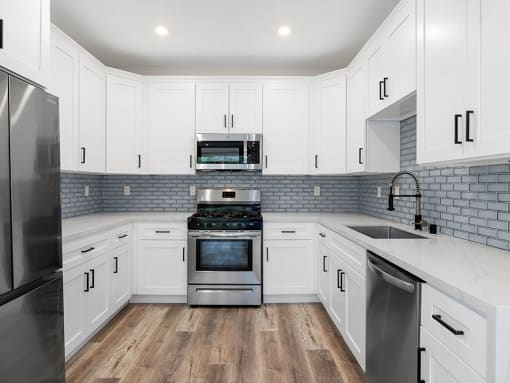 White tiled kitchen with stainless steel fridge, over, microwave, and fixtures.