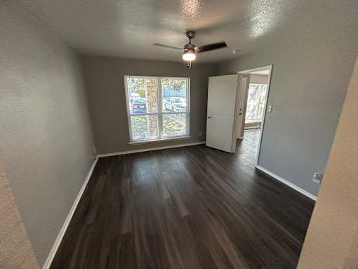 A room with a ceiling fan and a window with a view of cars and trees outside.