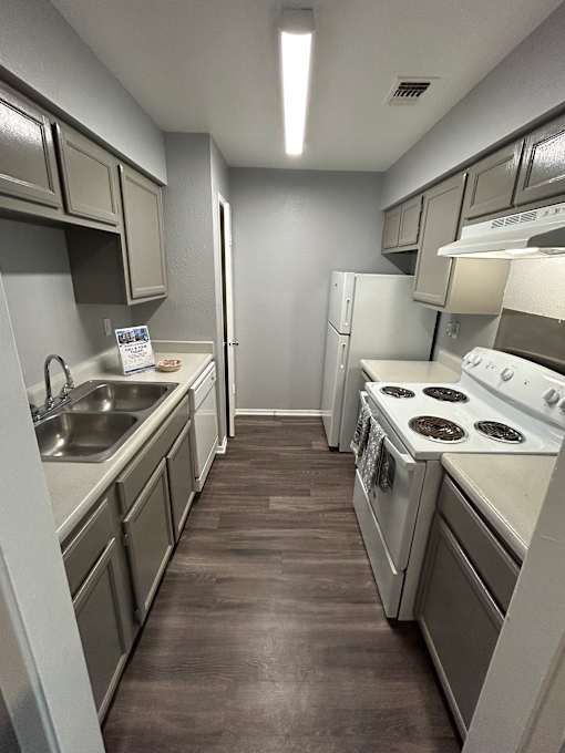 A kitchen with white appliances and a brown floor.
