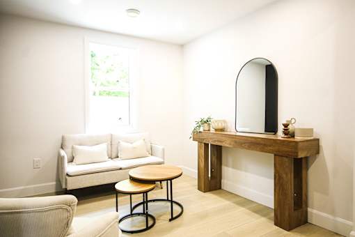A living room with a white couch, a wooden table, and a round chair.