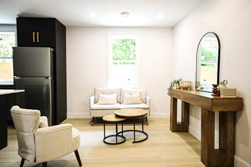 A black refrigerator stands next to a white chair in a room with a round table and a mirror.