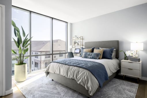 Interior photo of a typical bedroom in an apartment at RVR showing a queen sized bed with 2 night stands with dramatic floor to ceiling windows.,