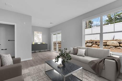 A modern living room with a grey couch, a glass coffee table, and a large window.