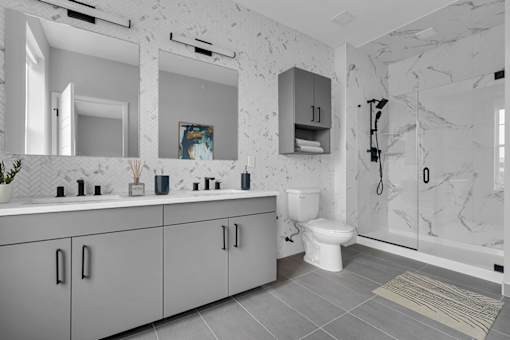 A bathroom with a marble wall and grey cabinets.