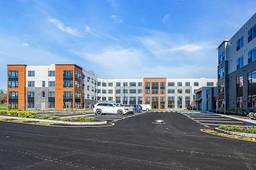 A parking lot in front of a multi-story building with cars parked.