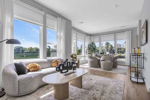 A modern living room with a grey sofa, a white coffee table, and a large window with a view of trees.