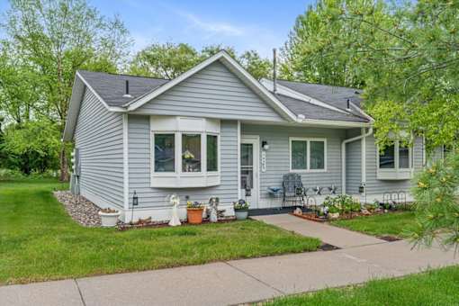 A house with a grey siding and a white door is surrounded by greenery.