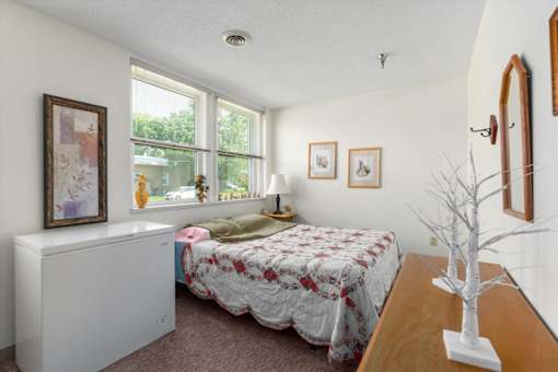 A bedroom with a bed, a window, and a picture on the wall.