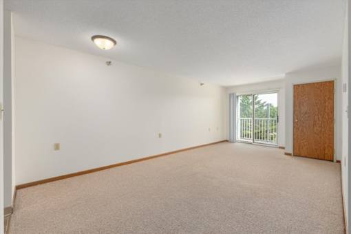 A room with a carpeted floor and a sliding glass door leading to a balcony.