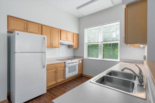 A kitchen with a white refrigerator, wooden cabinets, and a stainless steel sink.