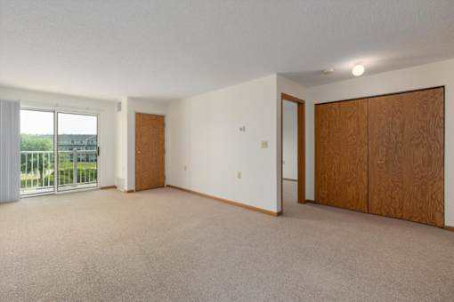A large empty room with a carpeted floor and a sliding glass door.