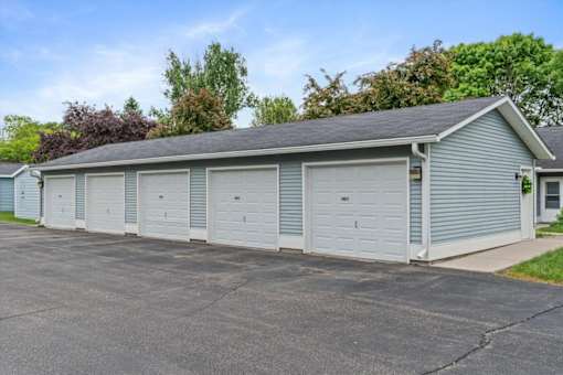 A long garage with four doors is surrounded by a driveway and a grassy area.