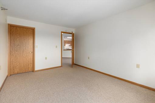 A room with a carpeted floor, a wooden door, and a mirror on the wall.
