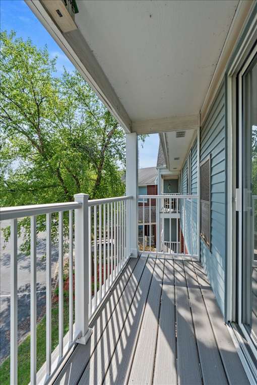 A white railing on a deck with a view of a tree and a house.