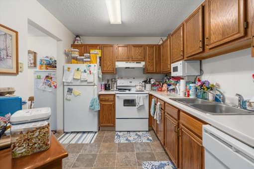 A kitchen with a white refrigerator, white dishwasher, white oven, and wooden cabinets.
