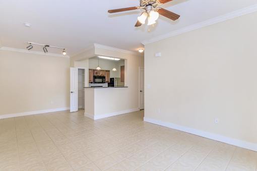 A spacious living room with a ceiling fan and a kitchen area in the background.