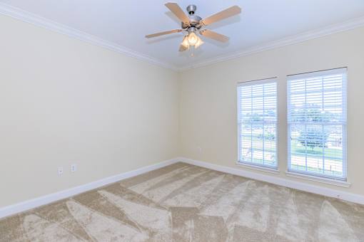 A room with a ceiling fan and two windows.