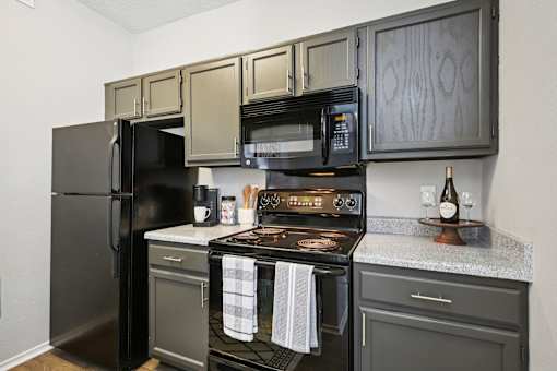 A black refrigerator is in a kitchen with a black stove and black microwave.