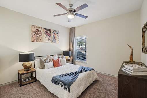 A bedroom with a bed, a ceiling fan, and a painting on the wall.