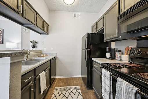 A kitchen with black appliances and wooden floors.