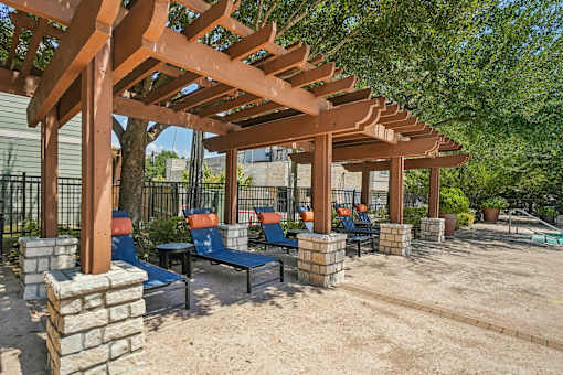 A wooden pergola with blue chairs and a sandy ground.