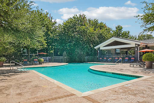 A large outdoor swimming pool surrounded by trees and a building.