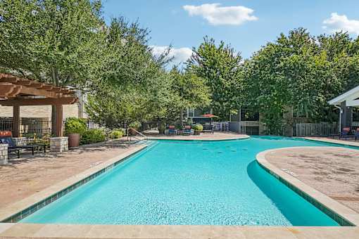 A large outdoor swimming pool surrounded by trees and a fence.