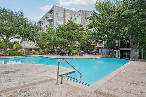 A swimming pool surrounded by trees and a building in the background.