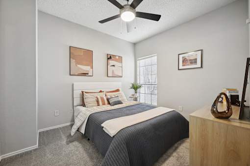 A bedroom with a bed, a ceiling fan, and a wooden nightstand.