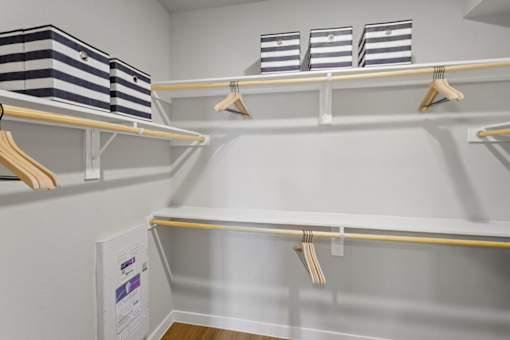 A white closet with clothes hanging and bins on the shelf.